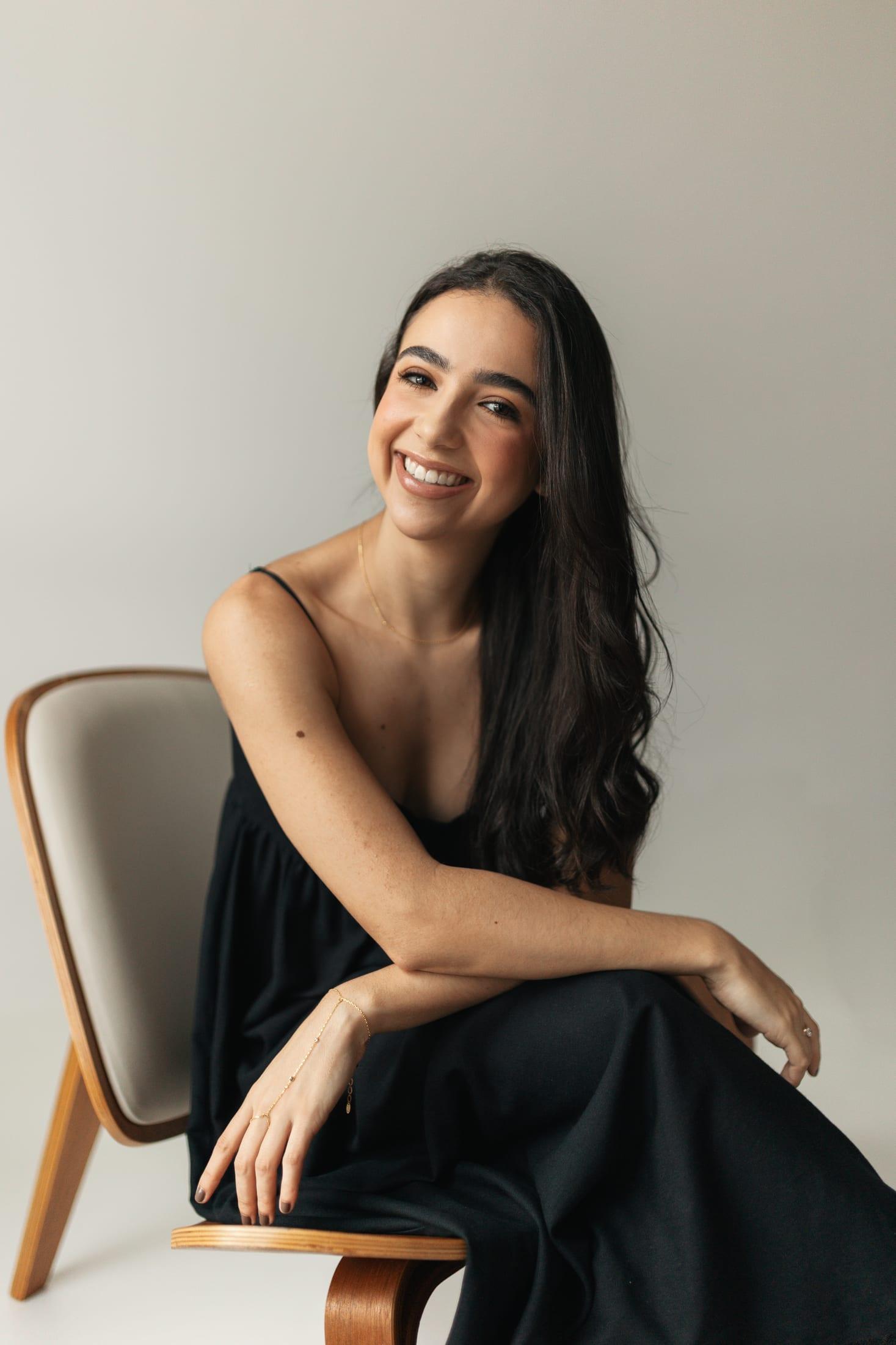 Dra. Larissa sentada em cadeira de madeira, sorrindo