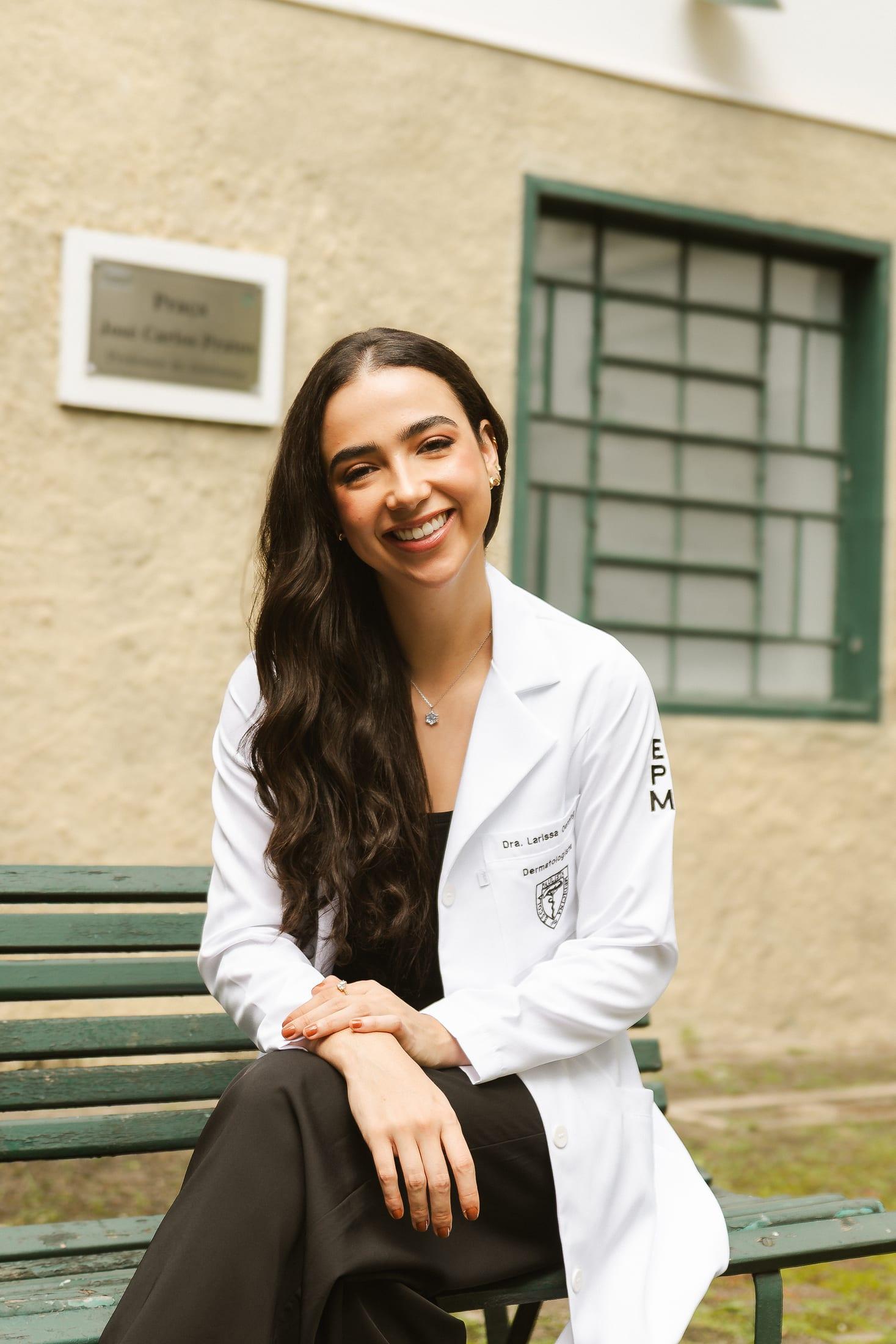 Dra. Larissa de jaleco sentada em um banco no campus da EPM